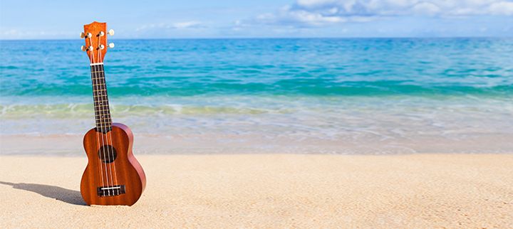 Ukelele laying on the beach with water in the background